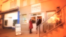 A screen grab of a woman and two young people entering a large beige building.
