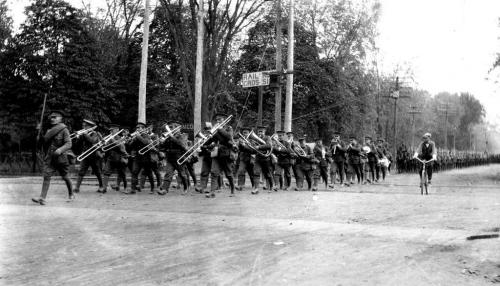 Une photographie en noir et blanc d’un groupe de soldats marchant au pas précédé d’un orchestre militaire de cuivres.