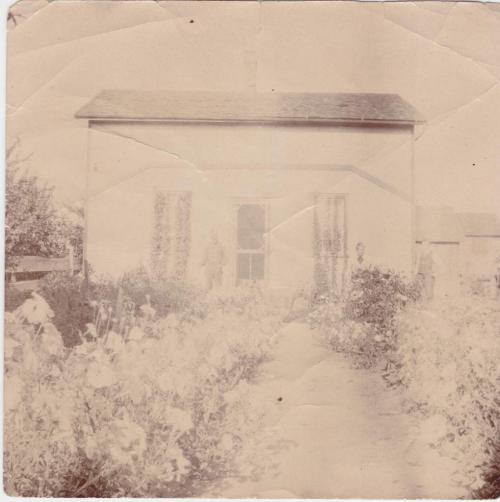 A photograph of a farmhouse with four people outside.