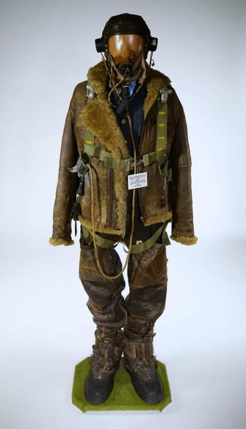 Un mannequin portant un casque d’écoute en cuir, un blouson aviateur  doublure épaisse et de grosses bottes.