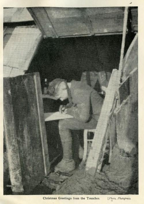 Une photographie en noir et blanc d’un soldat assis dans une tranchée en train d’écrire une lettre.