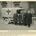 A black-and-white photograph of four people, including young Prince George, posing with a motorized ambulance.