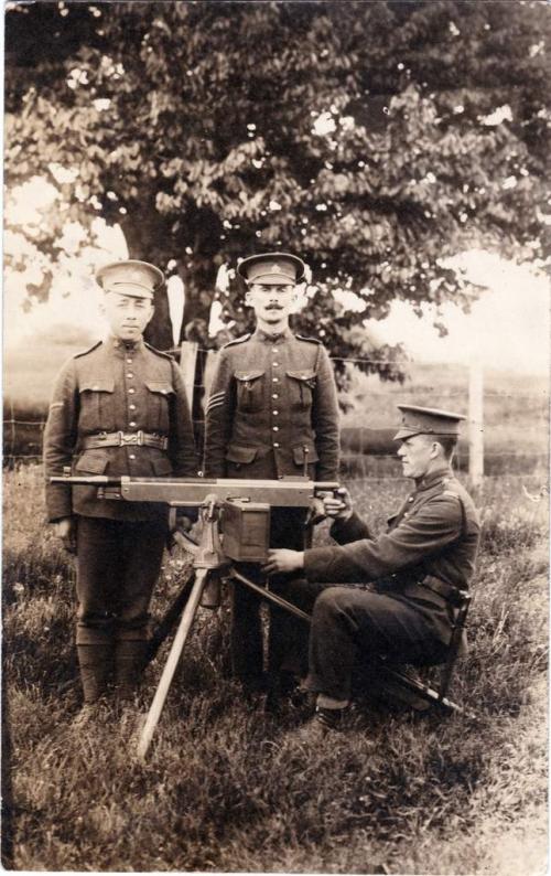 A photograph of two soldiers standing at attention behind a machine gun  manned by a sitting soldier.