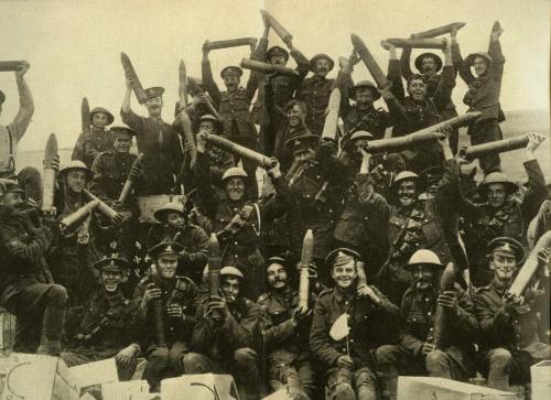A black-and-white image of a large group of Canadian soldiers happily hoisting   shells in the air.