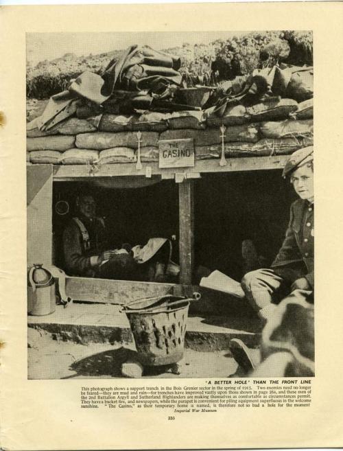 A black-and-white photograph of two soldiers sitting inside a well-constructed dugout in a trench.