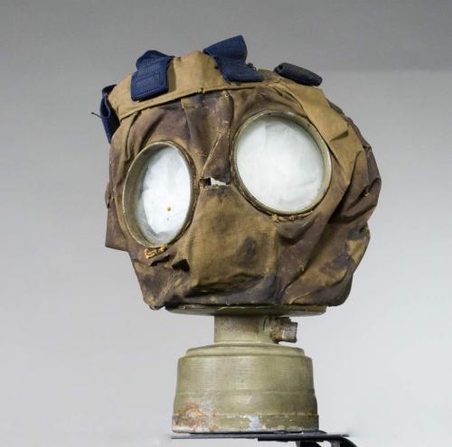 Un masque à gaz en toile avec des lunettes protectrices et une petite boîte en métal au bas.