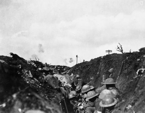A black-and-white image of soldiers in a trench with shrapnel bursting in background.