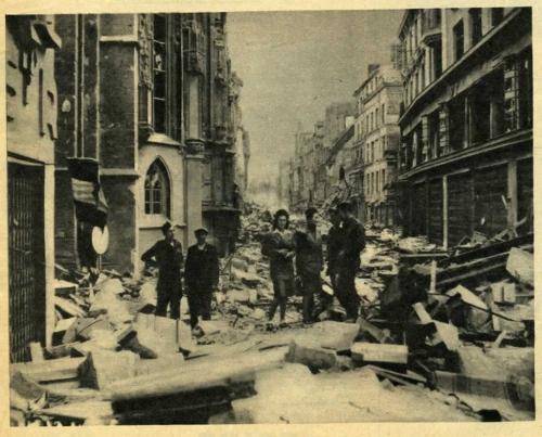 Une photographie en noir et blanc d’un civil et plusieurs soldats dans une ville bombardée.