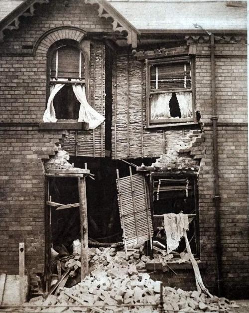 A photograph of a bombed two-story brick building with its front doors blown out.