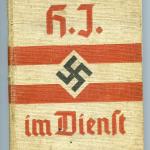 Un manuel relié beige avec de l’écriture rouge, deux rayures rouges et  une croix gammée noire au centre.
