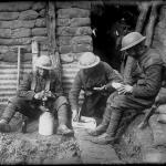 Trois soldats canadiens assis dans une tranchée en train d’ouvrir leurs paquets et de déguster leurs victuailles.