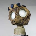 A canvas gas mask with goggle eyes and a small, metal canister on the bottom.