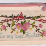 Une carte postale en tissu d’une église et d’une maison brodées adressée « À ma chère sœur ».